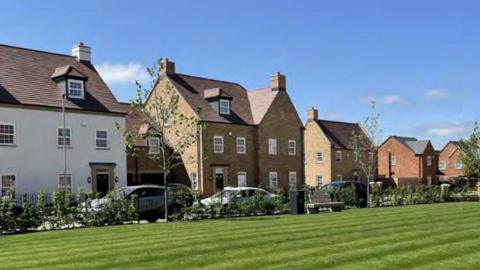 A row of modern houses of different designs. In the foreground is a green space.