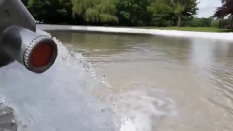 A photo taken from a video showing water going into a pool. Trees and grass are in the background.