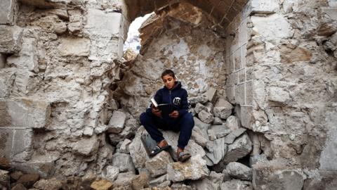 Boy sitting in rubble of historic site in Gaza