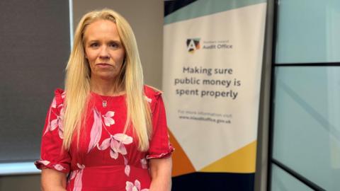 a woman with long blonde hair facing the camera. She is in front of a flipchart bearing the words Audit Office: Making sure public money is spent properly"