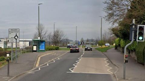 A stretch of road with a roundabout in the far distance and zig-zag lines on the road.