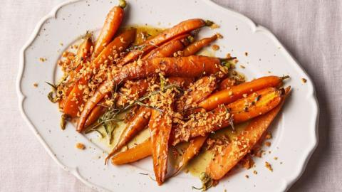 Braised carrots with a hazelnut crumb are spread out on a white, decorative plate.