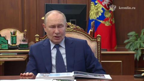 Putin, in a blue suit, shirt and tie, speaks from an ornate chair at a desk in the Kremlin