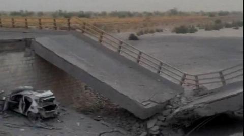 A damaged portion of the bridge in the aftermath of the overnight strike in Bandar Khamir, Hormozgan province. The image shows a portion of the bridge collapsed with rubble surrounding it, it is positioned diagonally with a damaged car