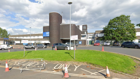 A large hospital building, with several vehicles parked in front 