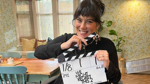 Kyla Harris holding a clap board reading 'We Might Regret This 2'