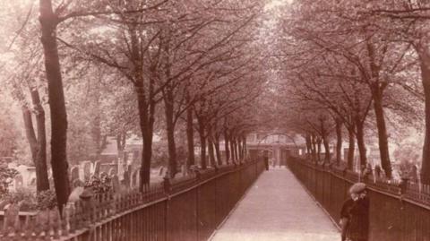 A brown photo of a cemetery with railings on both sides of a path that runs through the middle.