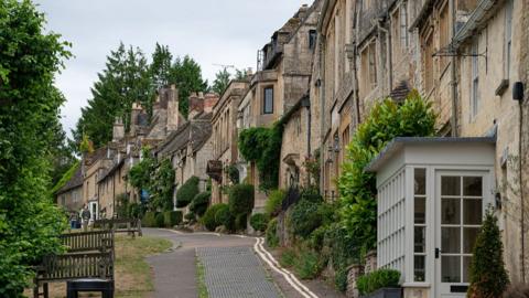 View of a street lined with properties and greenery in the town of Burford, UK.