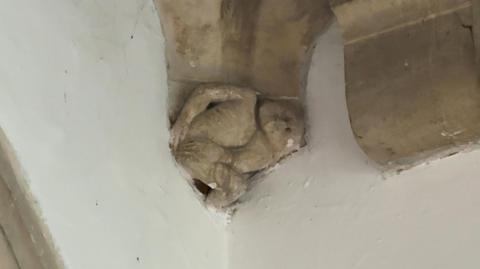 Stone carving of the imp at Grimsby minster. It is portrayed holding its bottom and at the bottom of one of the pillars supporting the tower.