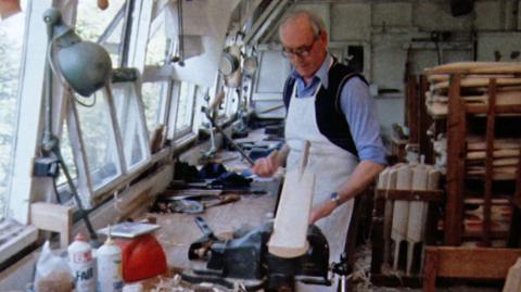 Man in a workshop handmaking a cricket bat. 