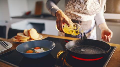Someone pouring oil into a frying pan.