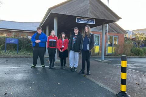 Four students with assistant head teacher Lydia Waite stand in front of the entrance to the school. 