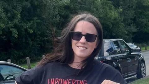 A woman with brown hair and sunglasses, wearing a black tshirt