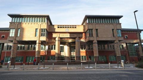 The exterior of Sheffield Crown Court, features red brick and ashlar stone and a three-storeys high central bay