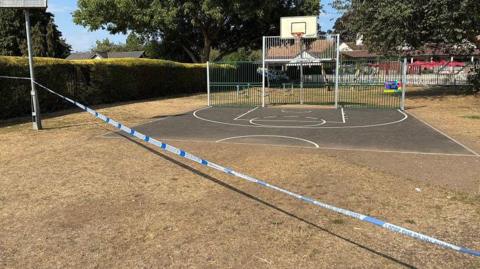 Blue and white police tape in front of a small basketball court.