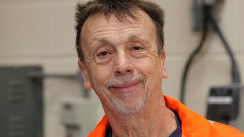 Nigel Brown smiling straight at the camera wearing an orange overall