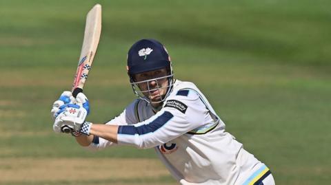 James Wharton, wearing a Yorkshire batting helmet and cricket whites, plays a shot