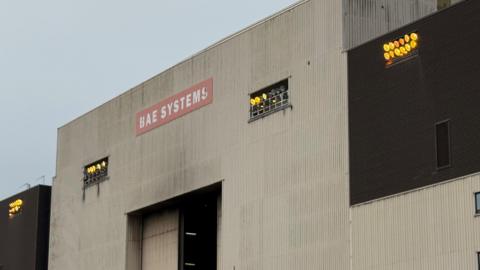 A white building with a red sign that reads: "BAE SYSTEMS". Grey and black streaks - smoke damage - can be seen on the exterior.