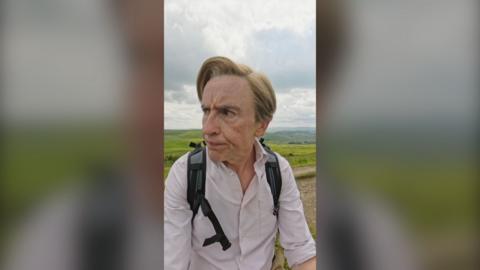 Steve Coogan character Alan Partridge standing on a hill looking quizzically to his side