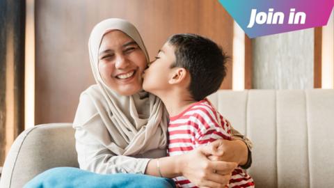 A little ball in a stripey red and white top kisses a woman's cheek while she hugs him, smiling with closed eyes at the camera