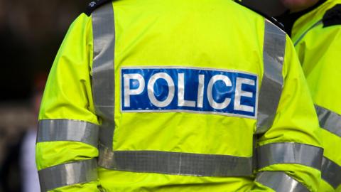 Close up of officer's with the words 'police' on. They are wearing a yellow high vis jacket. 
