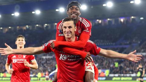 Chris Wood celebrates with his arms outstretched and Anthony Elanga jumping on his shoulders.