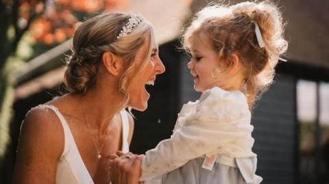 Sarah holds her daughter Lucy's hands as she smiles at her