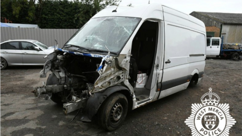 A white van in a car park with the front bonnet ripped off exposing the metal frame 