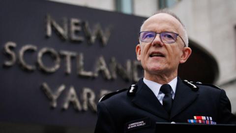 Sir Mark Rowley is seen in uniform speaking in front of the New Scotland Yard sign.