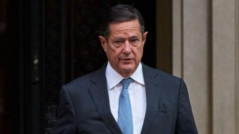 Jes Staley emerging from a doorway wearing a suite and a pale blue tie