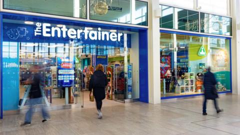 The Entertainer store front in an indoor shopping centre with blurred customers walking past