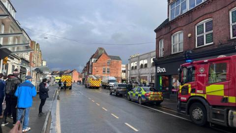 Baxter Street in Loughborough with emergency vehicles parked at the side of the road, either side of police tape which is stretched across the highway.