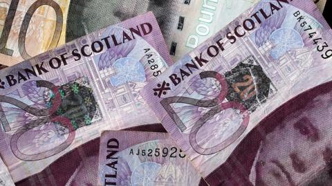 An arrangement of Scottish pound sterling banknotes are spread on a table top 