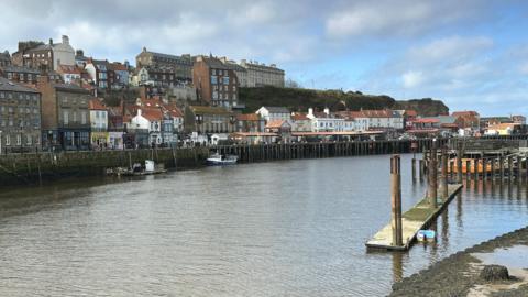 Whitby harbour with houses and shops on one side and several fishing boats moored up 