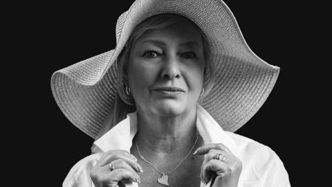 Woman wearing a large sunhat, white shirt and a heart necklace with a black and white filter over the picture.