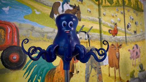 A blue plastic cartoon-style octopus on a pole with an IV bag hanging off one tentacle.