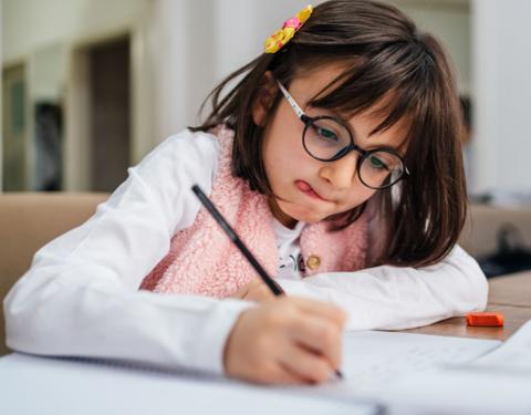 Young girl in glasses in deep concentration writes a short story for the 500 Words competition.