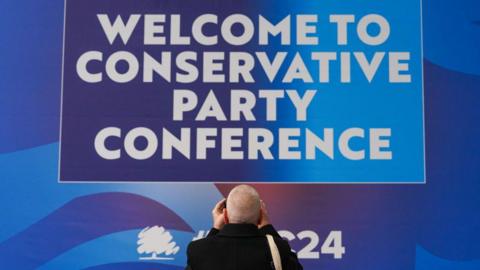 A delegate takes a photo of the welcome sign at the second day of the Conservative Party Conference at Birmingham ICC Arena