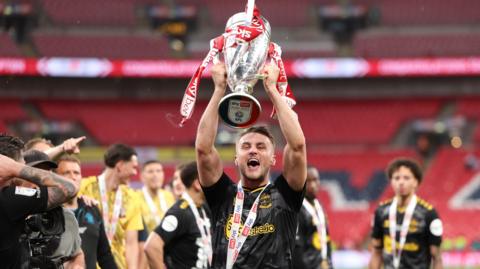 Taylor Harwood-Bellis holds the Championship play-off final trophy aloft