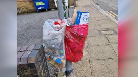 Bin bag tied to a lamp post in the street full of rubbish 