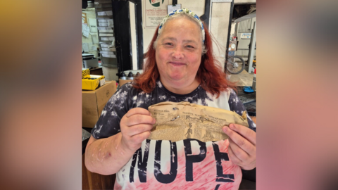 A woman holding a scrap of old newspaper.