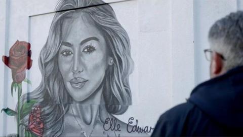 Tim Edwards can be seen from the back looking at a tribute mural to his daughter Elle Edwards. A rose and butterfly have been added to a black and white image of her.