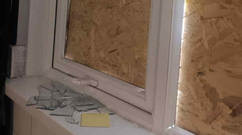 Two boarded up windows with shards of glass visible on a window pane