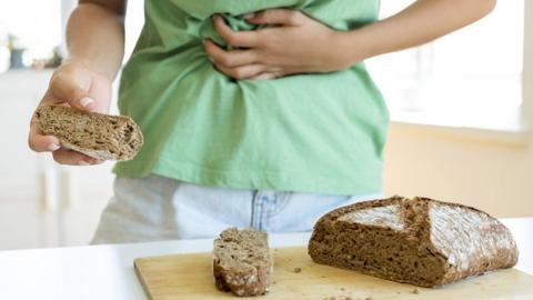 A person holding their stomach whilst holding a piece of bread