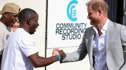 Prince Harry outside a recording studio grasping the hand of a man