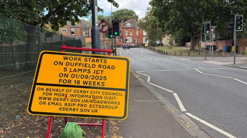 A sign reading "work starts on Duffield Road 5 Lamps junction on 1st September for 16 weeks" next to the road.