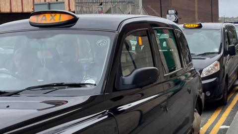 Two black taxi cabs parked in a row near Sheffield train station.