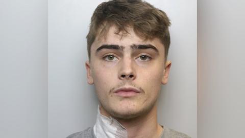 Police mugshot of Alfie Franco, with brown wavy air and a moustache. He has a white bandage on the right side of his neck.