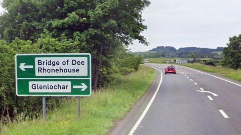 Road with a red car on it beside some bushes and a road sign saying bridge of dee.
