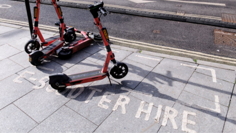 E-scooters on a pavement which has the words 'e-scooter hire' printed on 